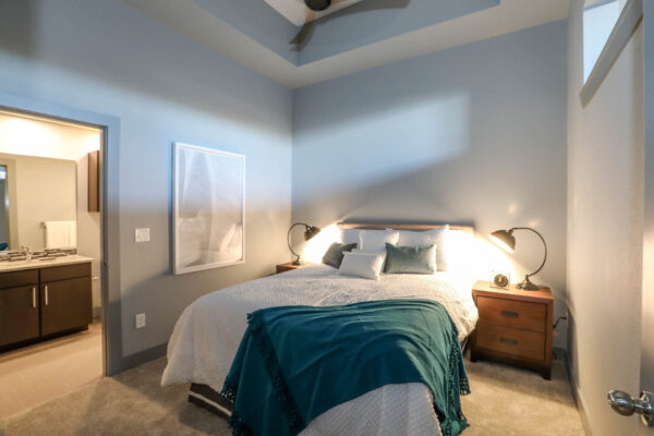 Forum Fitzsimons apartment bedroom with carpet, plush bed with headboard, bedside tables with lamps, and vaulted ceiling.
