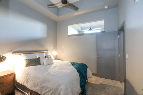 Forum Fitzsimons apartment bedroom with carpet, plush bed with headboard, bedside tables with lamps, and ceiling fan.