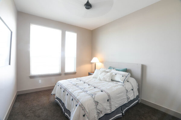 Forum Fitzsimons apartment bedroom with carpet, plush bed with headboard, ceiling fan, and large windows.