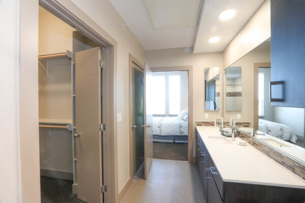 Forum Fitzsimons apartment bathroom with dark cabinets, light counters, large mirror, and closet door.