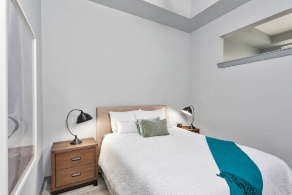 Forum Fitzsimons apartment bedroom with carpet, plush bed with headboard, and bedside tables with lamps.