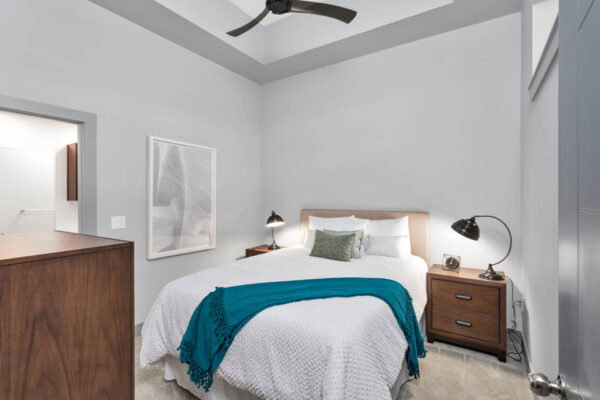 Forum Fitzsimons apartment bedroom with carpet, plush bed with headboard, and bedside tables with lamps.
