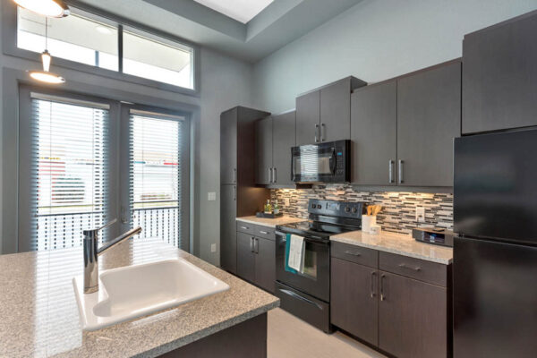 Forum Fitzsimons apartment kitchen with dark cabinets, light counters, and black appliances.