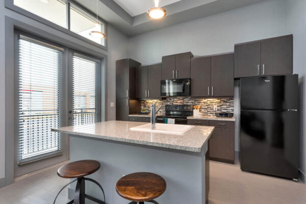 Forum Fitzsimons apartment kitchen with dark cabinets, light counters, and black appliances.