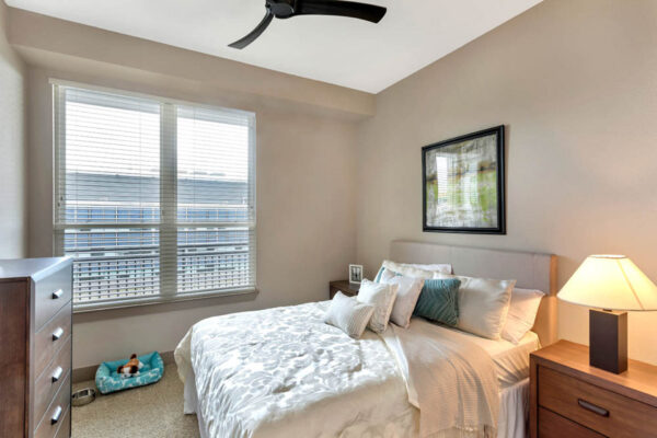 Forum Fitzsimons apartment bedroom with carpet, plush bed with headboard, bedside tables with lamps, and large window.