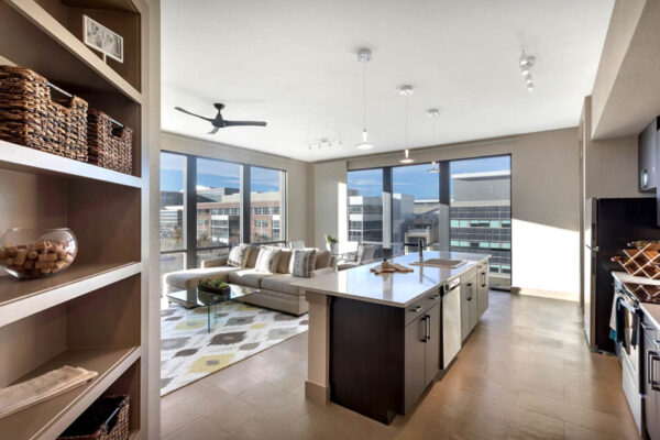 Forum Fitzsimons apartment living area with modern kitchen, plush seating, and built in shelves.