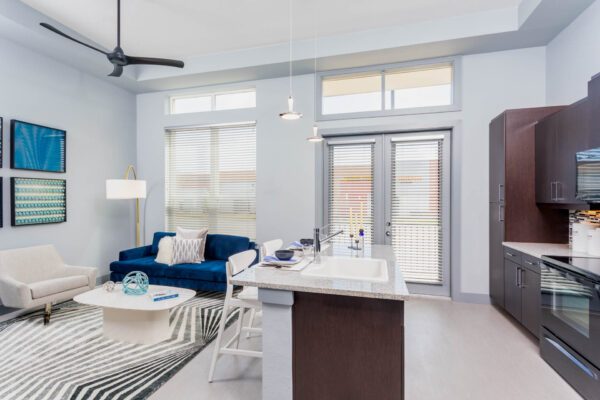 Forum Fitzsimons apartment living area with plush seating, modern kitchen, and large windows.