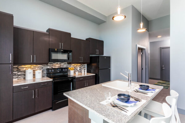 Forum Fitzsimons apartment kitchen with dark cabinets, light counters, and black appliances.