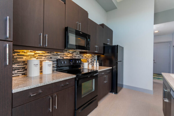 Forum Fitzsimons apartment kitchen with dark cabinets, light counters, tiled backsplash, and stainless steel appliances.