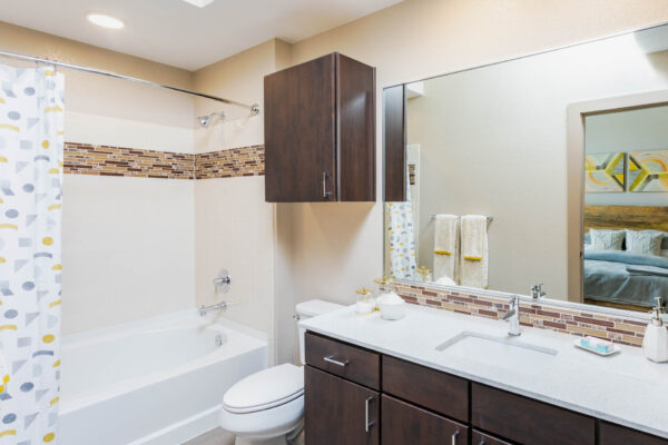 Forum Fitzsimons apartment bathroom with dark cabinets, light counters, and tiled shower tub.