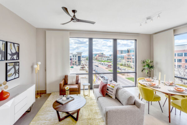 Forum Fitzsimons apartment living area with ceiling fan, plush seating, elegant dining, and large windows.