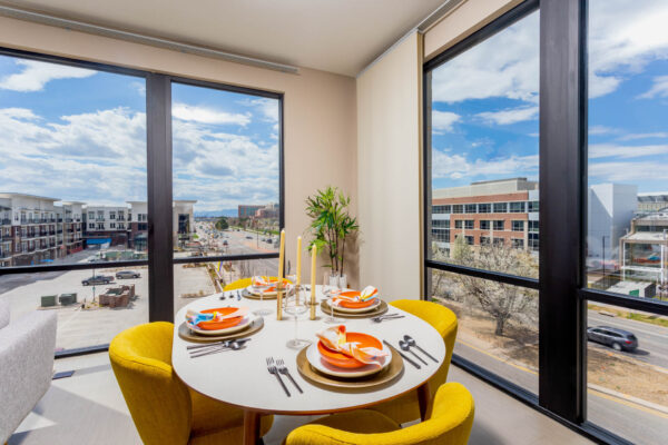 Forum Fitzsimons apartment dining area with elegant table and chairs and large windows.