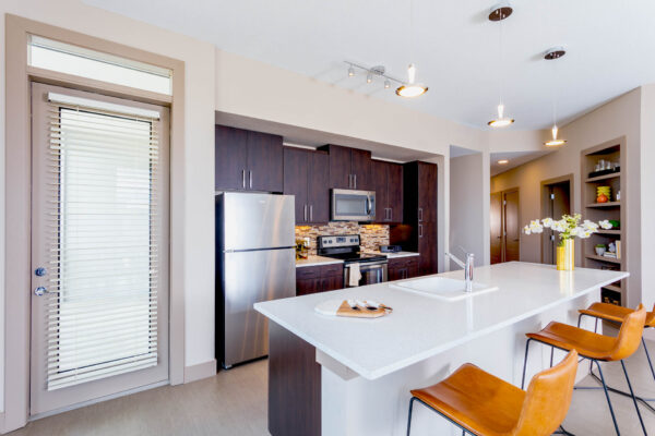 Forum Fitzsimons apartment kitchen with dark cabinets, light counters, and stools.