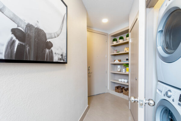 Forum Fitzsimons apartment hallway with framed art, built in shelves with decor, and laundry closet.