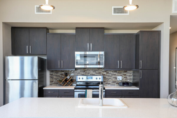 Forum Fitzsimons apartment kitchen with dark cabinets, light counters, stainless steel appliances, and pendant lights.