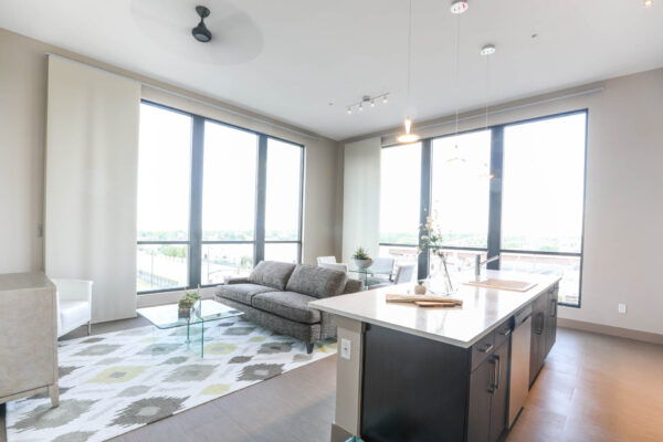 Forum Fitzsimons apartment living area with kitchen island, plush seating, and large windows.
