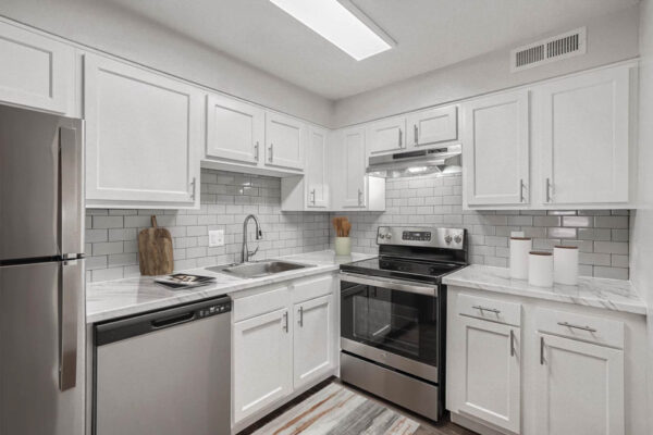 Heights on Huron apartments kitchen with wood style floors, white cabinets, marbled countertops, tiled backsplash and stainless steel appliances.
