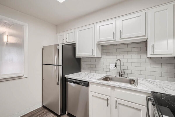 Heights on Huron apartments kitchen with wood style floors, white cabinets, marbled countertops, tiled backsplash and stainless steel appliances.