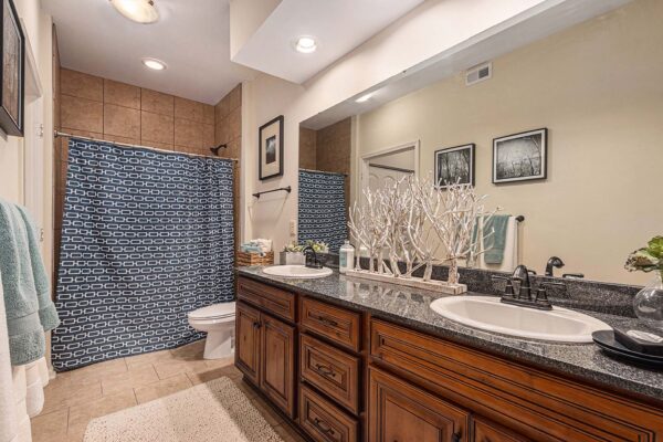 Highlands Lodge apartment bathroom with tile floor, wood cabinets, stone counters, and large mirror.