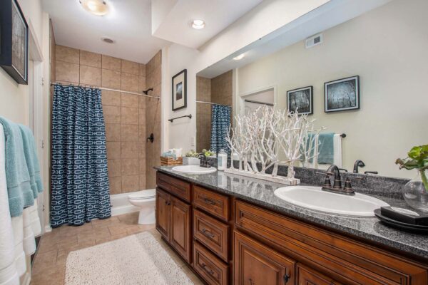 Highlands Lodge apartment bathroom with tile floor, wood cabinets, stone counters, and tiled shower.