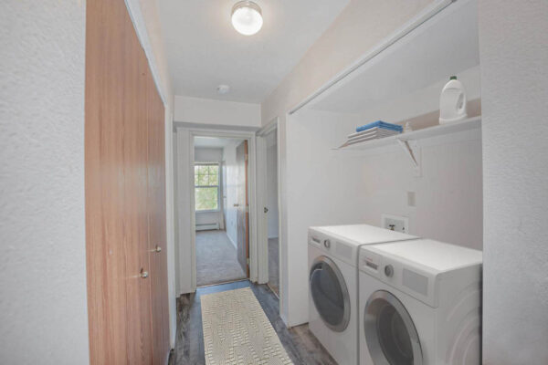 Mountain Village apartments laundry area with wooden floors, washer, dryer, and built in shelf.