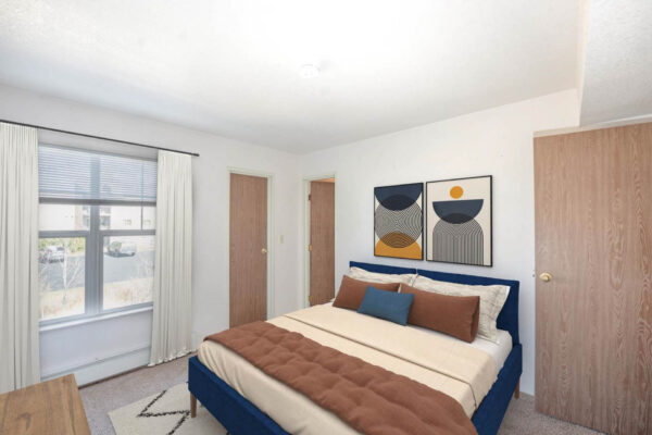 Mountain Village apartments bedroom with carpet, bed with plush headboard, large windows and wooden doors.