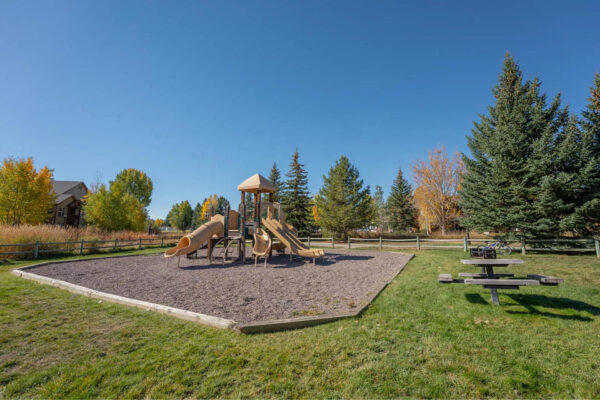Mountain Village apartments playground with wood fencing, picnic table and big trees.