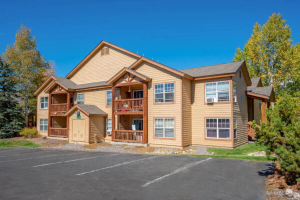 Mountain Village apartments buildings with balconies, big trees and parking lot area.