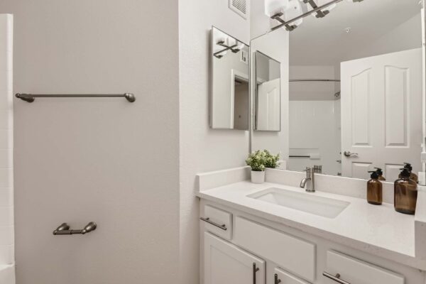 Pavilions at Arrowhead apartment bathroom with white cabinets and counters, large mirror, and light fixture.
