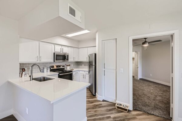 Pavilions at Arrowhead apartment kitchen with wood style floor, white cabinets and counters, and stainless steel appliances.