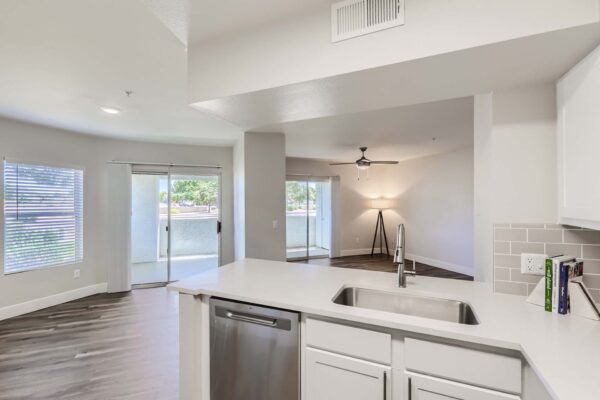 Pavilions at Arrowhead apartment living area with wood style floor, modern kitchen, ceiling fan, and balcony doors.