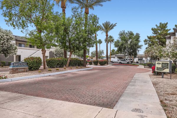 Pavilions at Arrowhead apartments driveway with stone pavers and lush trees.