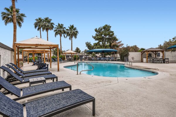 Pavilions at Arrowhead apartments pool area with lounge chairs, gazebos, and umbrellas.
