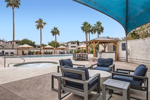 Pavilions at Arrowhead apartments pool area with hot tub, outdoor seating, and large shade sail.