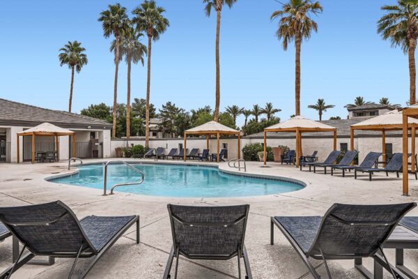 Pavilions at Arrowhead apartments pool area with lounge chairs, gazebos, and tall palm trees.