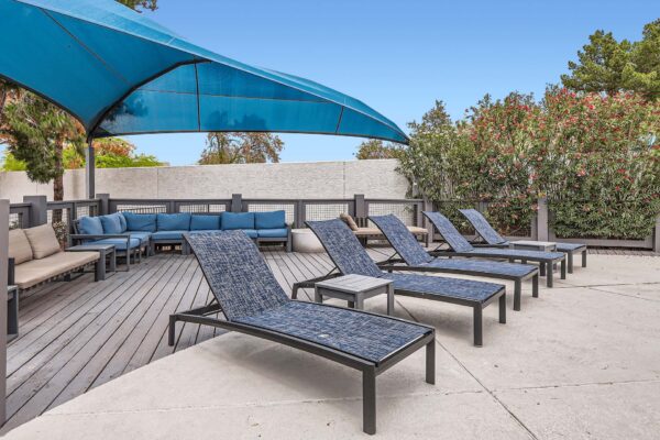 Pavilions at Arrowhead apartments pool area with lounge chairs and large shade sail.