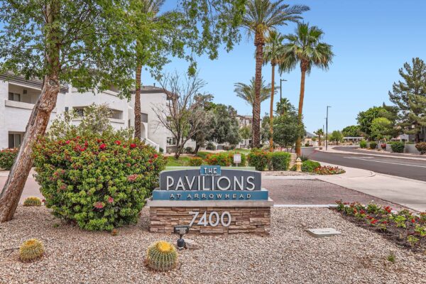Pavilions at Arrowhead apartments driveway with monument sign and rocky landscaping.