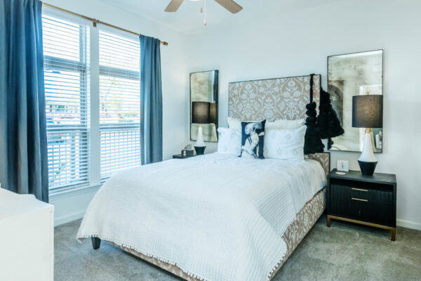 Residence at Old Hickory Lake apartments bedroom with dark style nightstands, large window, ceiling fan and abstract artwork.