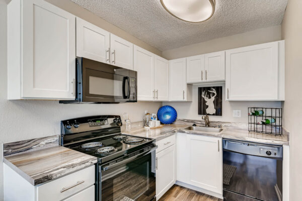 Sunset Peak apartments kitchen with white walls and wood like flooring, featuring black kitchen appliances and white cabinets