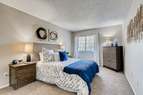 Sunset Peak apartment bedroom with carpet, plush bed with headboard, bedside tables with lamps, and large window.