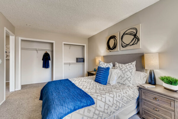Sunset Peak apartment bedroom with carpet, plush bed with headboard, bedside tables with lamps, and large closets.