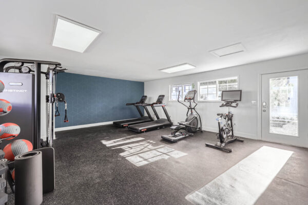 Sunset Peak apartments indoor fitness center featuring cardio equipment, a multi-functional weight machine, dumbbells, resistance bands, and exercise balls