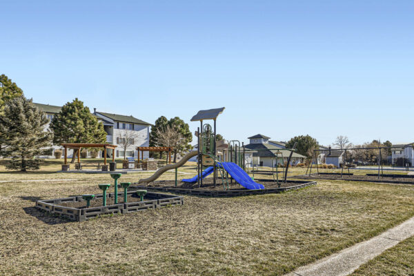 Sunset Peak apartments grassy outdoor area with a playground featuring green swings, a slide, and climbing structures.