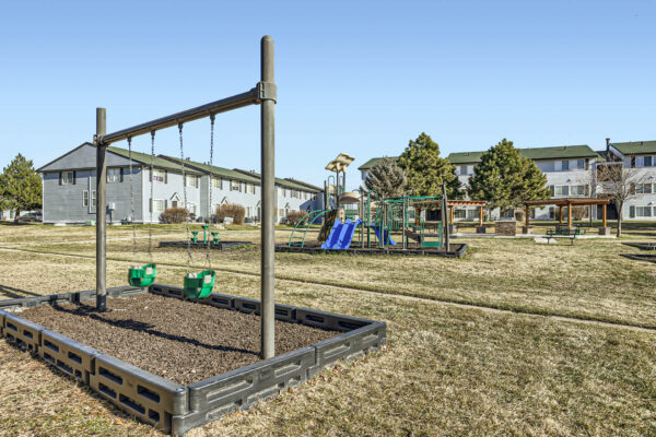 Sunset Peak apartments grassy outdoor area with a playground featuring green swings, a slide, and climbing structures.