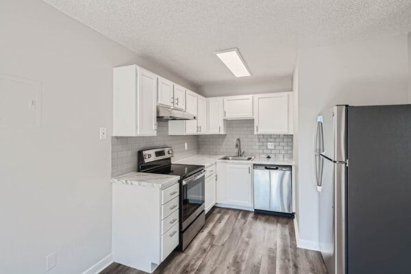 Sunset Peak apartments kitchen with white walls and gray wood like flooring, featuring a modern electric stove, white cabinets, and white tile backsplash