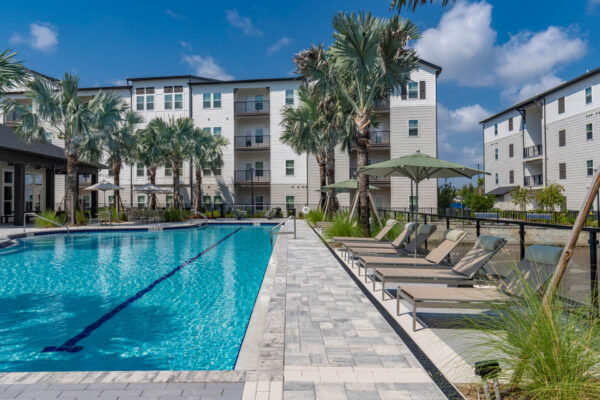 The Avery apartments pool area with lounge chairs, umbrellas, and palm trees.