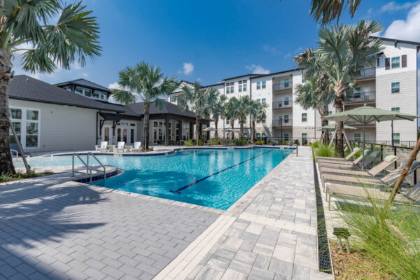 The Avery apartments pool area with lounge chairs, umbrellas, and palm trees.