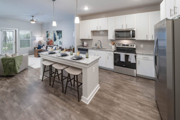The Avery apartment kitchen with wood style floor, white cabinets, stone counters, and stainless steel appliances.