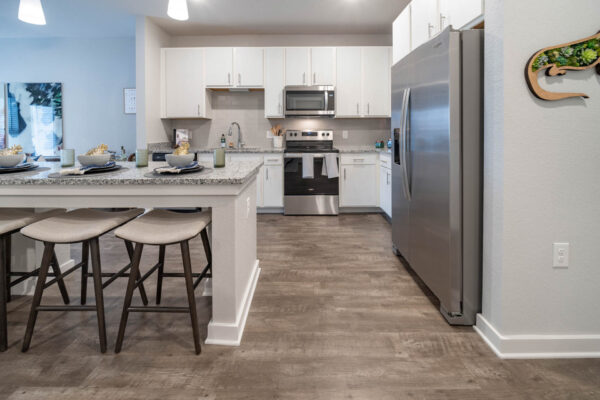The Avery apartment kitchen with wood style floor, white cabinets, stone counters, and stainless steel appliances.