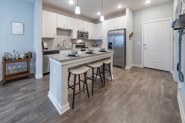 The Avery apartment kitchen with wood style floor, white cabinets, stone counters, and stainless steel appliances.